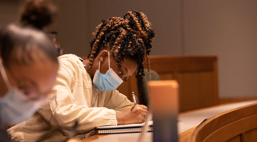A Suffolk student wears a mask while taking notes in Sargent Hall.