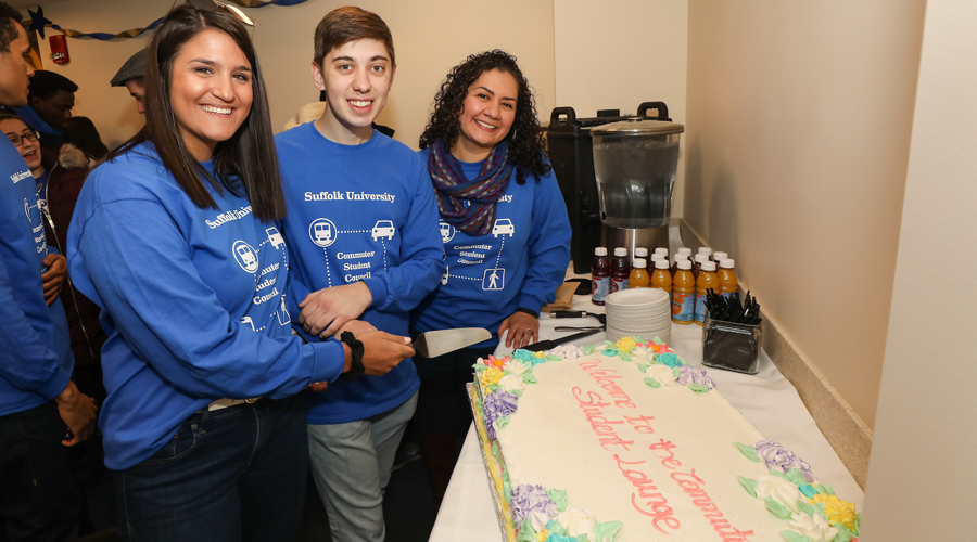 Suffolk student Alexia poses while cutting a cake at the Commuter Student Lounge opening.