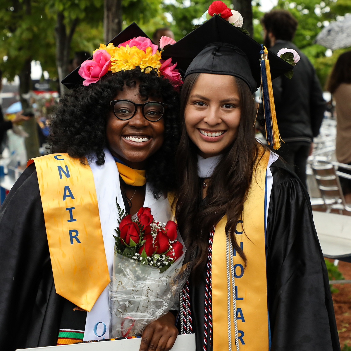 Arly posing for a photo with a friend wearing her cap and gown following Commencement.