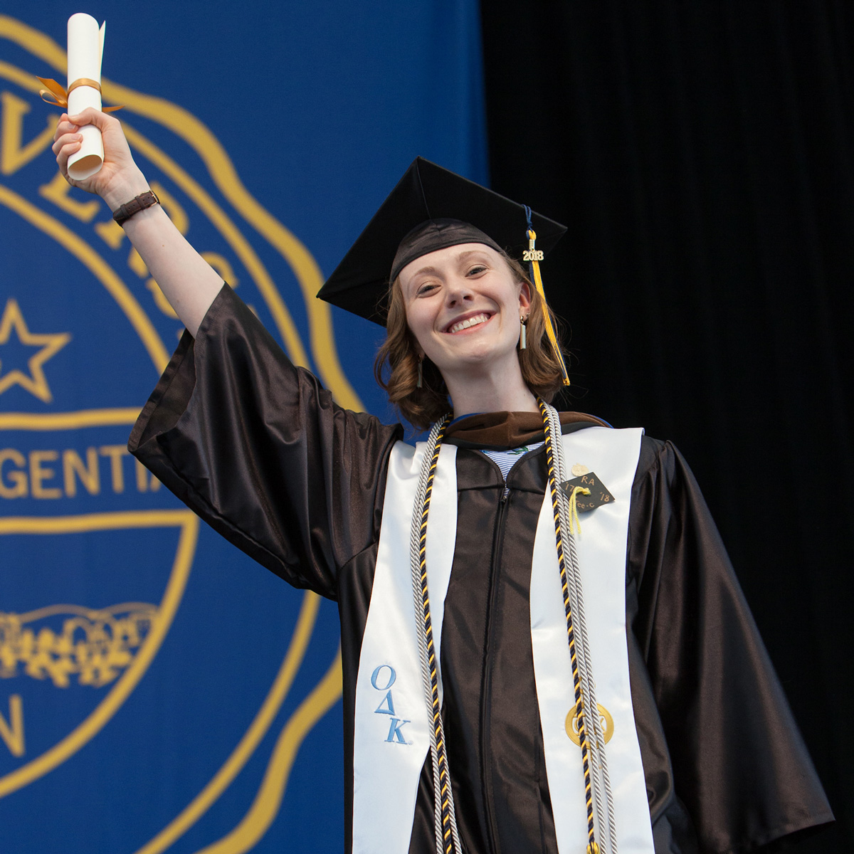 Brianna wearing her cap and gown while holding up her scroll on stage at Commencement.