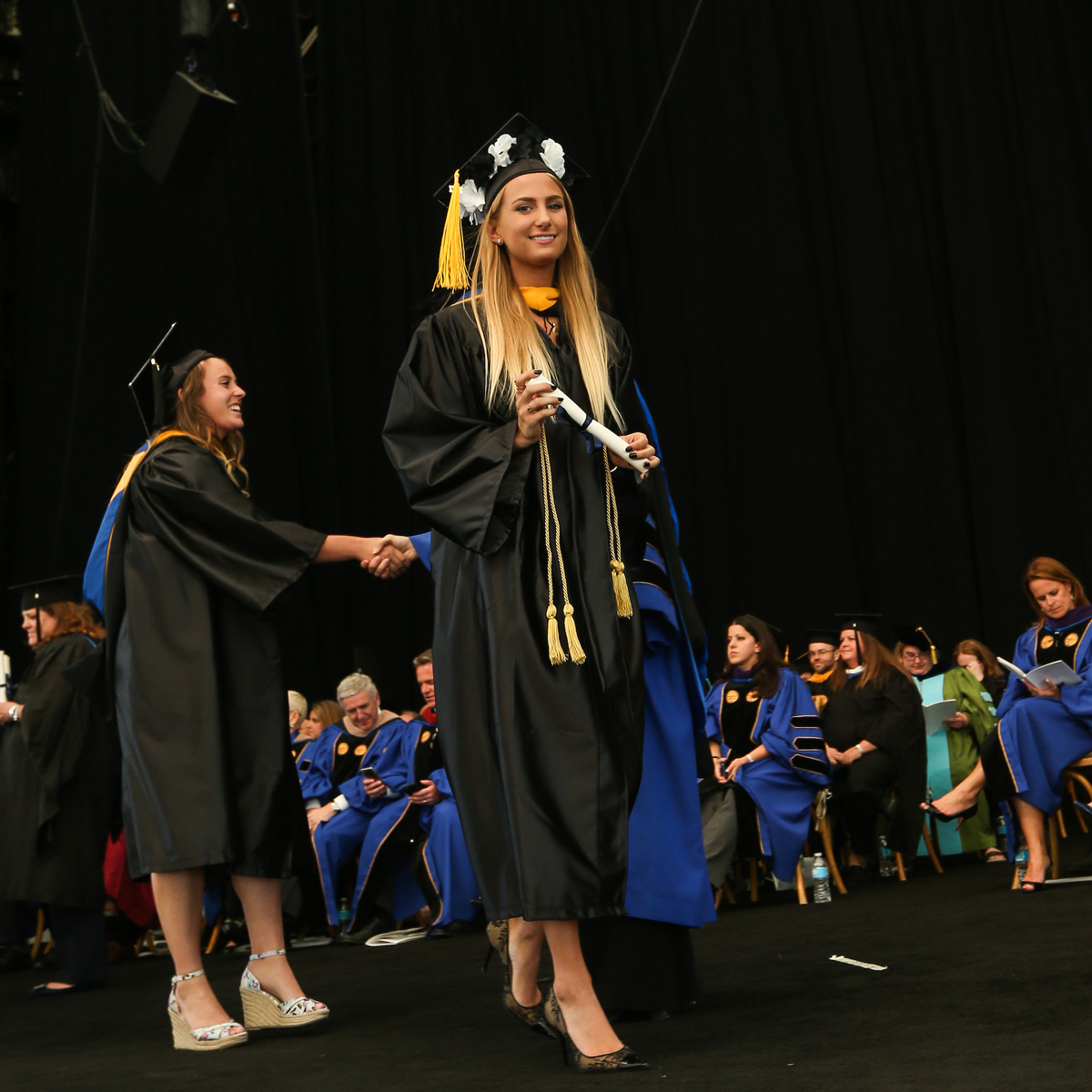 Casey Parker smiling for the camera while crossing stage in her cap and gown during Commencement.