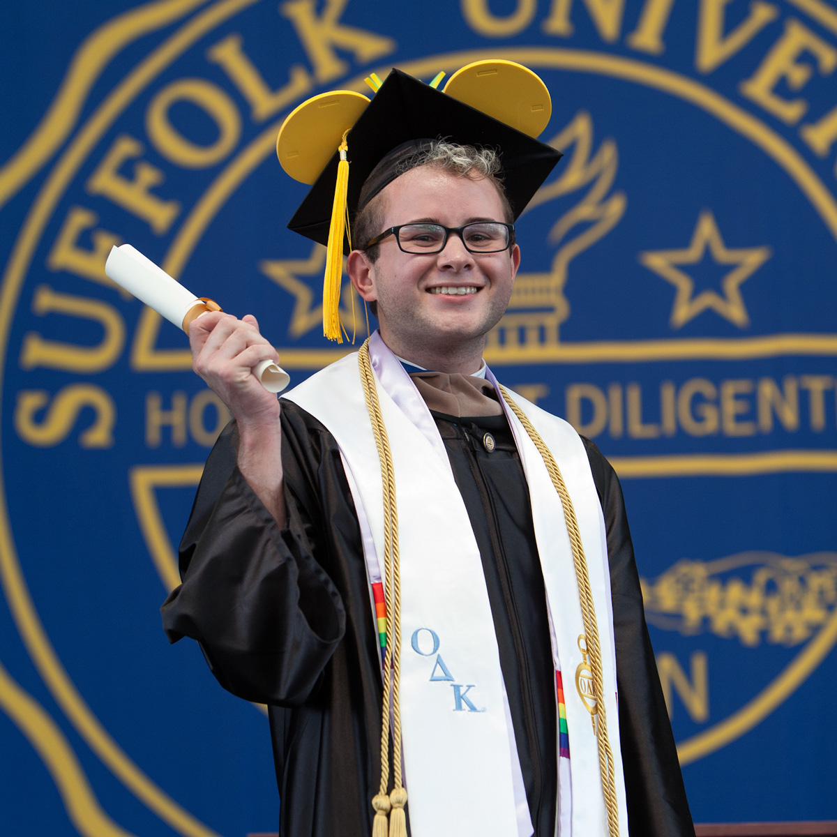 Kevin holding up his scroll wearing his cap and gown crossing the stage at Commencement.