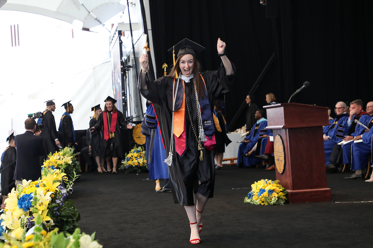 Laurel celebrates, holding her scroll high, as she walks across the stage at Commencement.