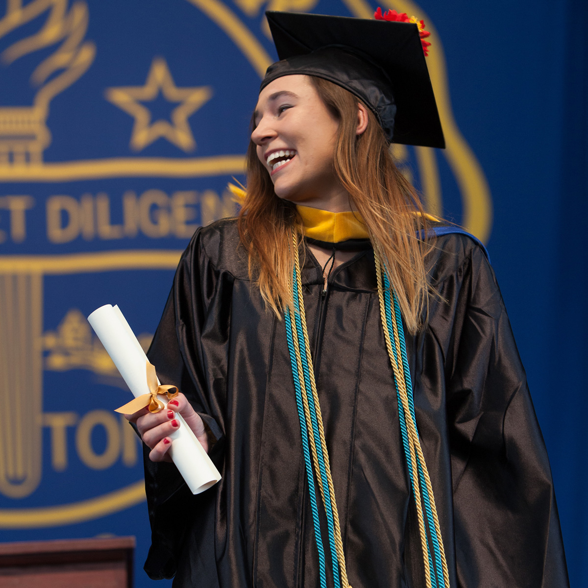 Olivia smiling while holding her scroll in her cap and gown crossing the stage at Commencement.