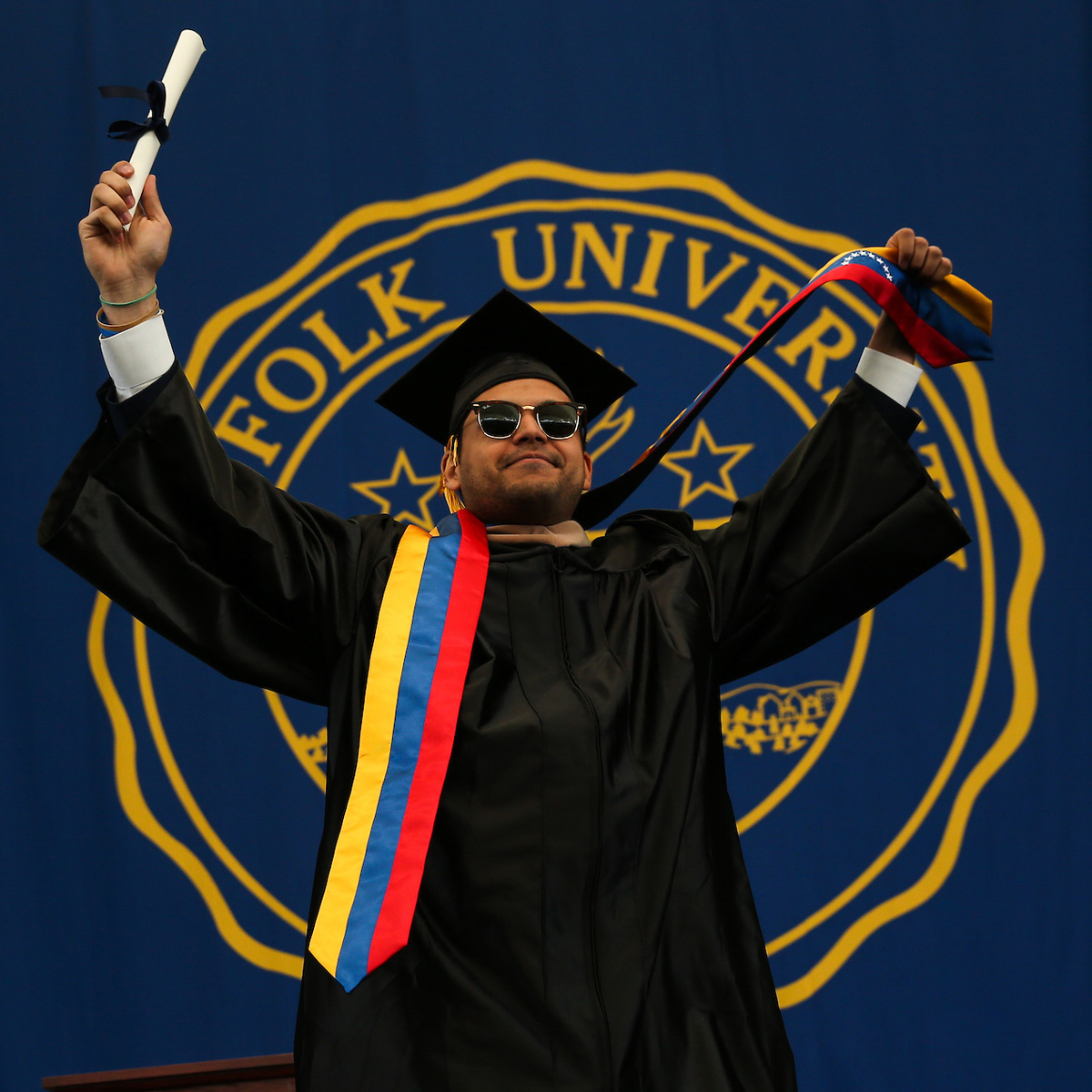 Omar Hernandez proudly displaying his scroll and Venezuelan flag on stage during Commencement.