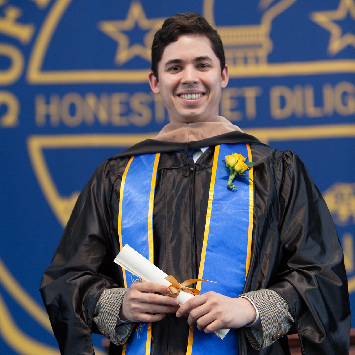 Rafael Sanchez holding his scroll on stage during Commencement ceremonies.