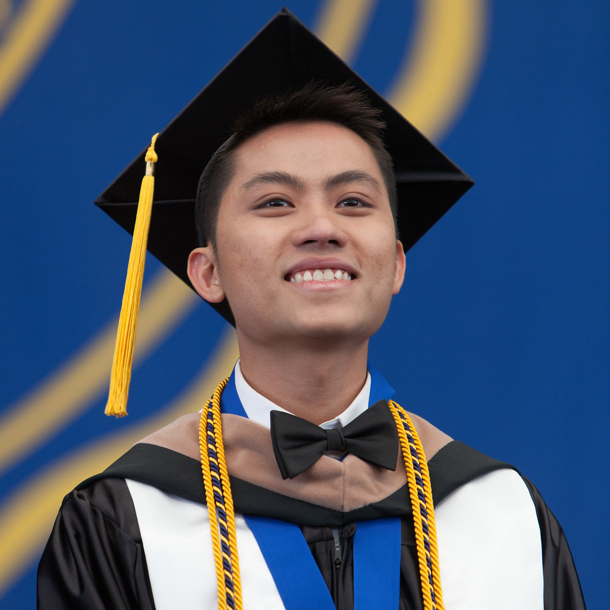 Tyler La smiling in his cap and gown on stage during Commencement.