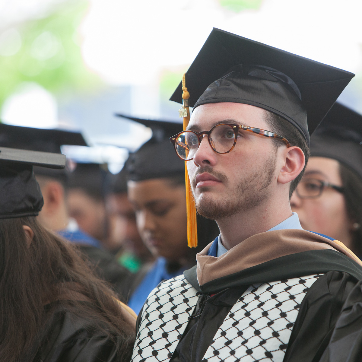 Yazeed Abu-Ghazaleh in his cap and gown sitting in the crowd during Commencement.