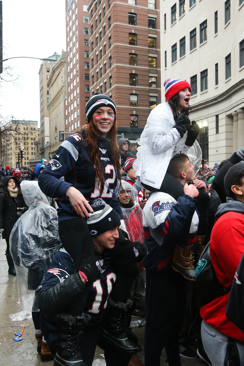 Patriots fans look on as their team's victory parade flows by Suffolk University's Sargent Hall.