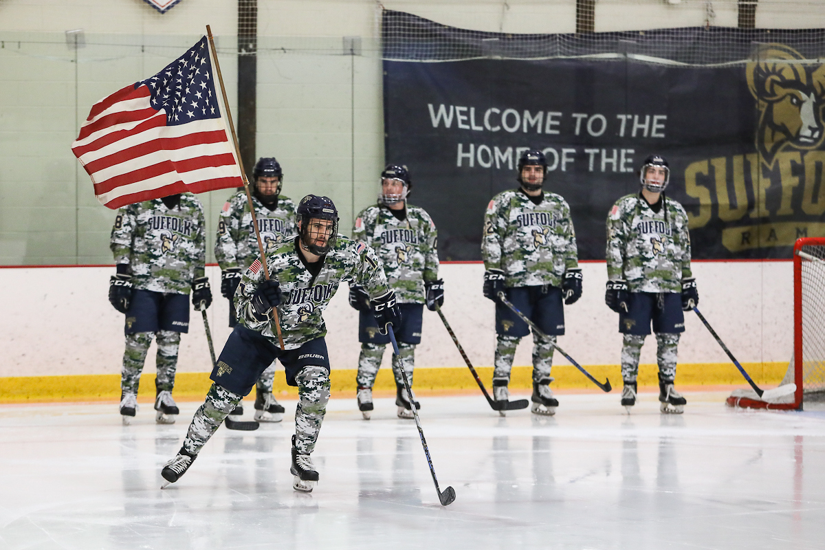 Suffolk hockey player skating while holding American flag. 