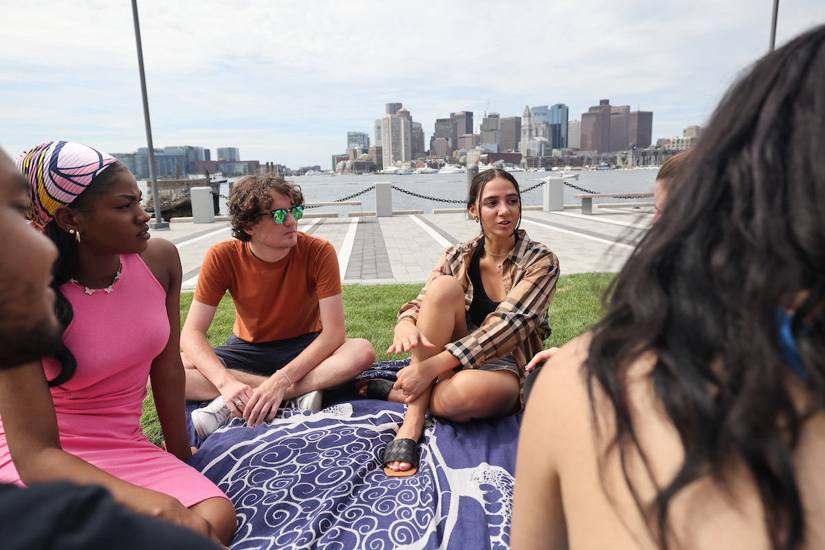 Suffolk students sit on a blanket and talk while enjoying the East Boston waterfront.