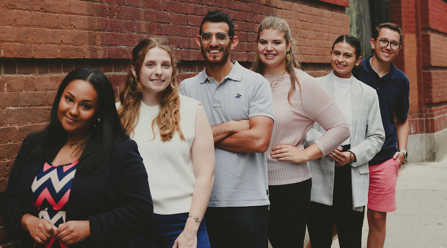 Suffolk students pose for a portrait against a brick wall in the North End of Boston.