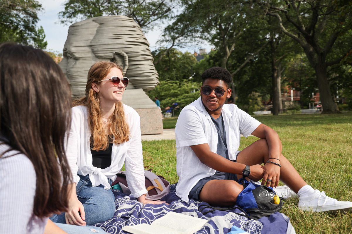 Suffolk students Chloe and Vinny sit together on a blanket on the Charles River Esplanade in Boston.