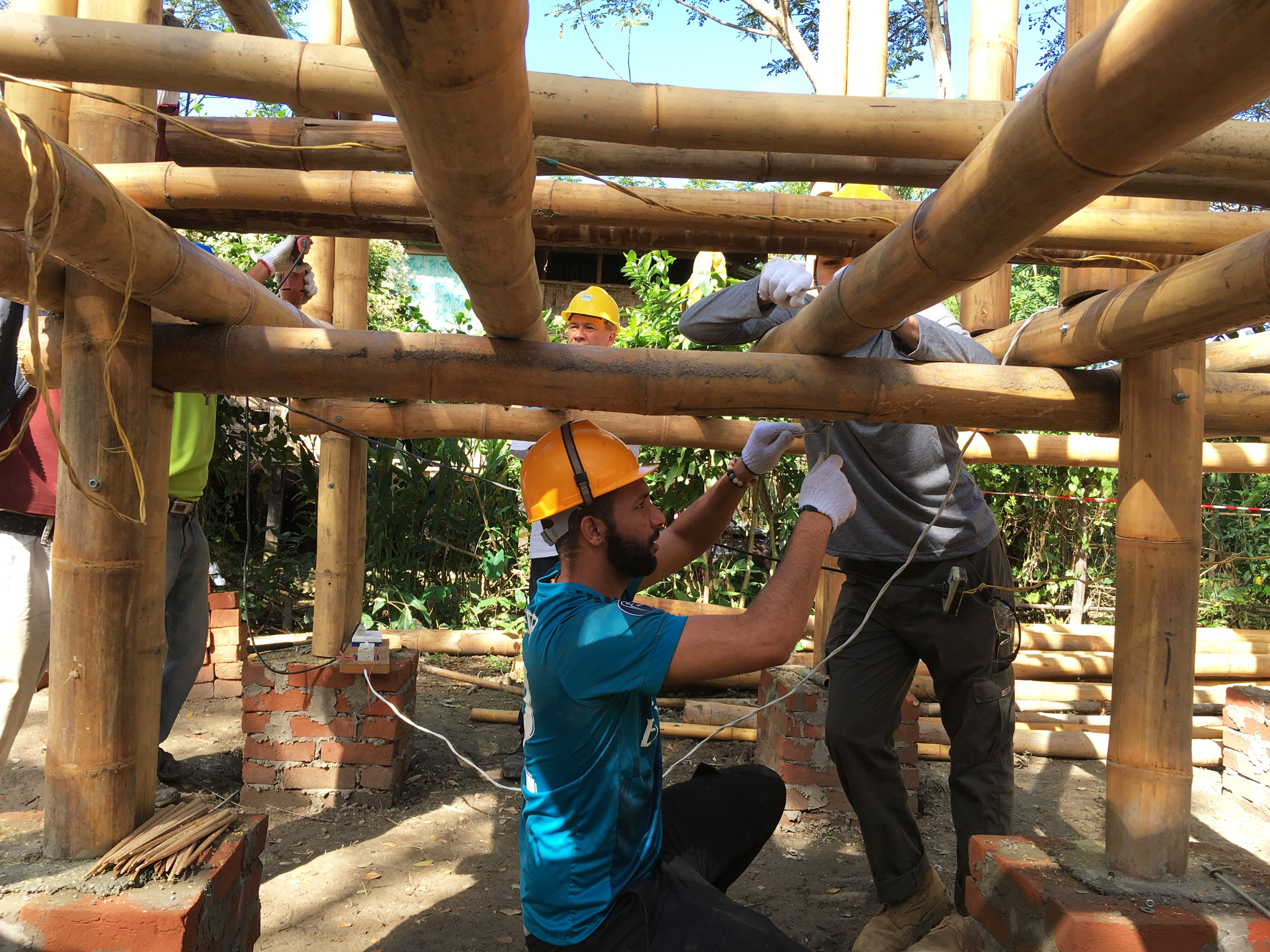 Two Suffolk students adding electrical wires to the bamboo frame of a new home.