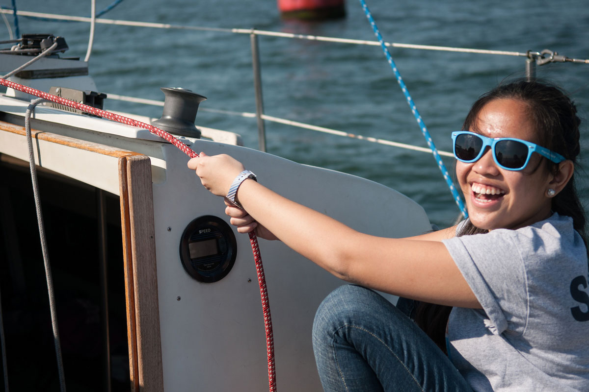A Suffolk Journey student smiles for the camera as she pulls tight a rope during her sailing lesson.