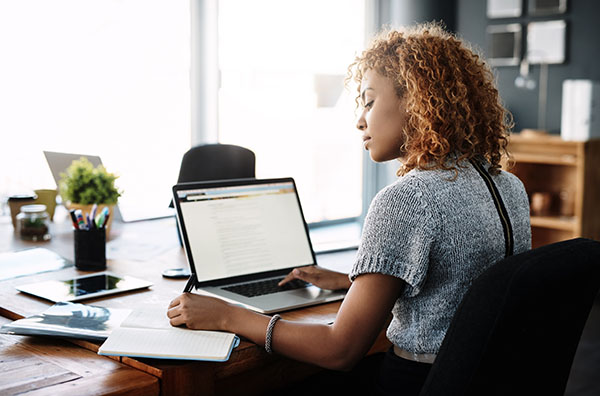 Woman at desk working with laptop and taking notes on paper