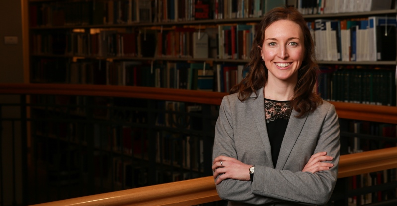 Suffolk Law student Anne Marie Beliveau standing in front of a railing and the library book stacks