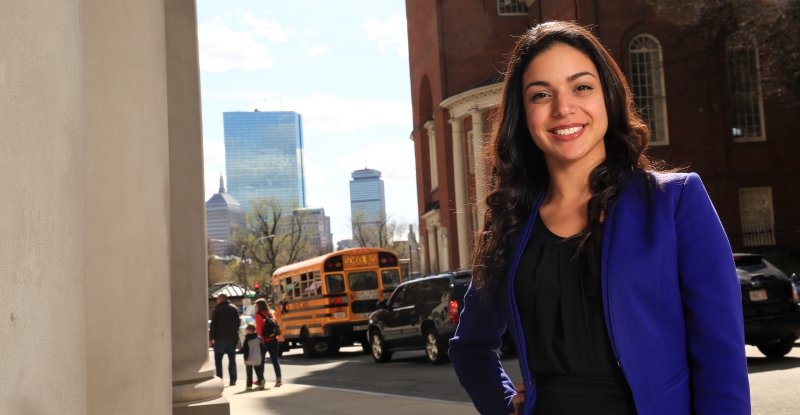 Priscilla Guerrero standing along Tremont Street in front of the law school with the city skyline behind