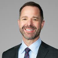 Bearded, brown haired Todd Boudreau smiling with black jacket, grey tie, and light blue shirt