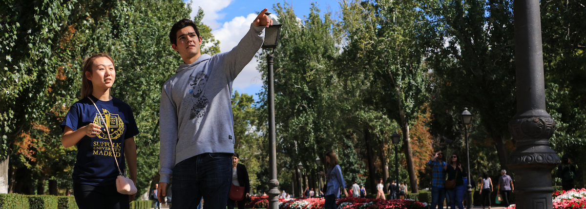 Two Suffolk Madrid students walk together while one points our something to the other.