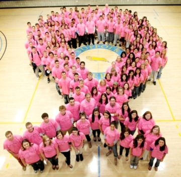 Students and staff standing in the shape of a ribbon all wearing pink t-shirts 