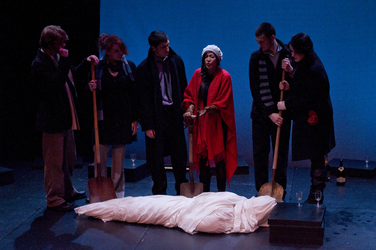 Group of actors surronding a dead body with shovels 