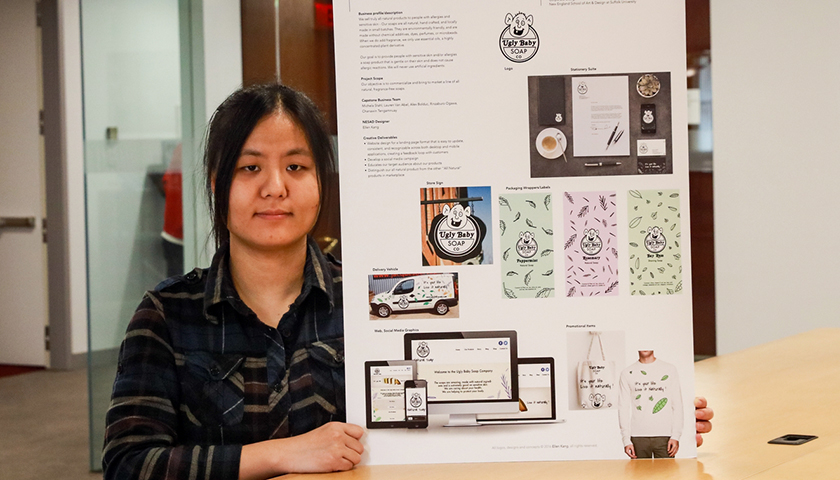 Ellen Kang holds a poster showing her design plan for Ugly Baby soap, featuring a drawing of a bald, big-eared baby whose smile shows one tooth