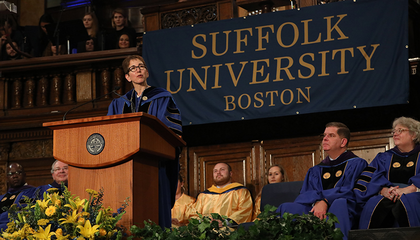 Marisa Kelly, wearing royal blue academic robe, speaking at podium