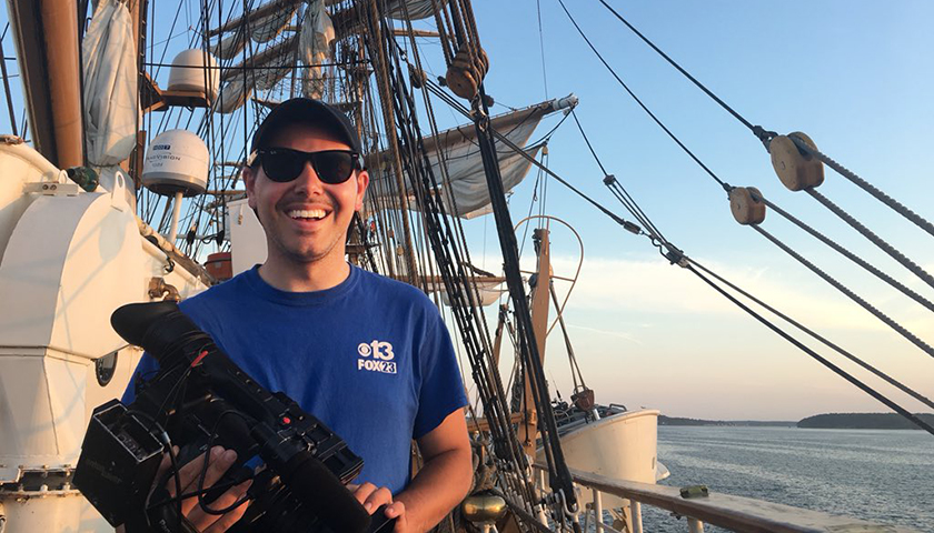 Dan Lampariello holding video camera with mast of tall ship in background