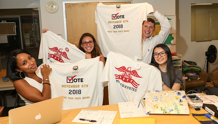 Students at voter registration table hold up Suffolk Votes T-shirts