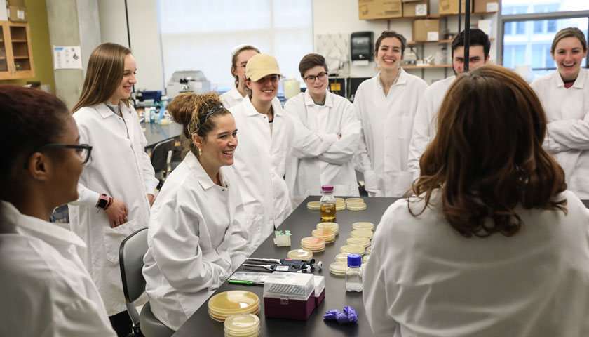 Artist in the lab discussing process with students in lab attire