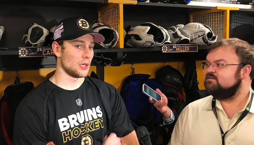 Brandon Carlo in Bruins team shirt interviewed by Tim Rosenthal holding microphone