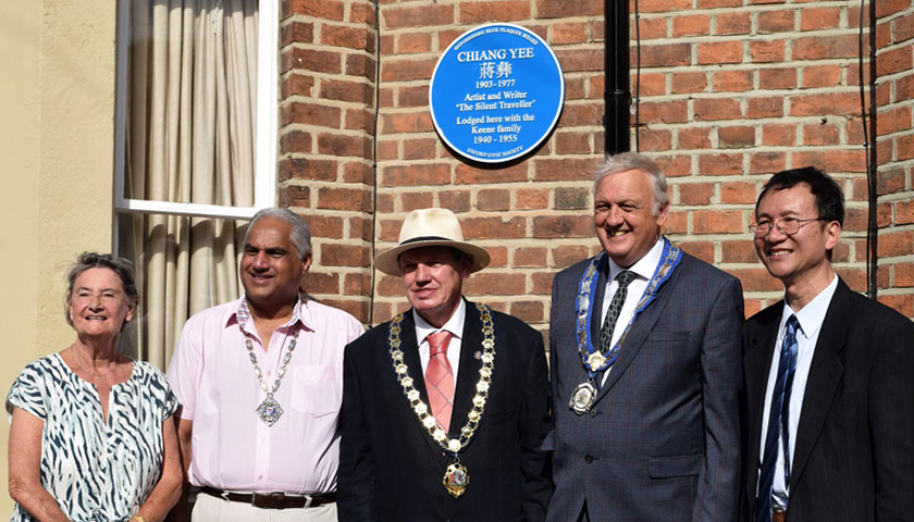 Group of people pose in front of red brick house with blue plaque