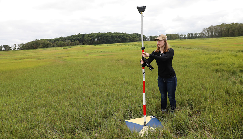 Student holds places pole holding monitoring instrument in center of target to mark geolocation