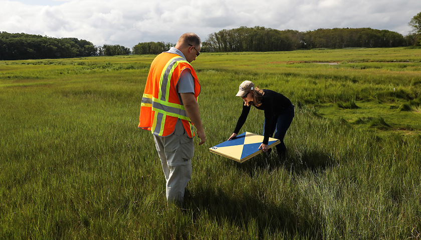 Student bends to set target atop marsh grass as Lussier offers guidance
