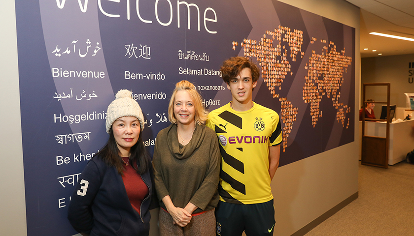 Yucong Xu, Kathy Sparaco, and Felipe Giesteira in front of sign saying welcome in many languages