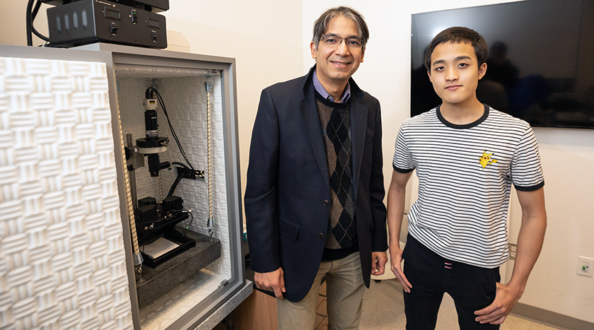 Professor Prashant Sharma Calvin Kem standing next to microscope