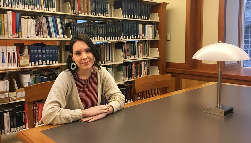 Katelyn Hubbard sitting at library table with shelves full of books behind her