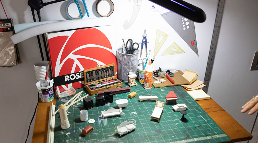 Model of design setup with tiny furniture, rulers, exacto knives, tape and other tools