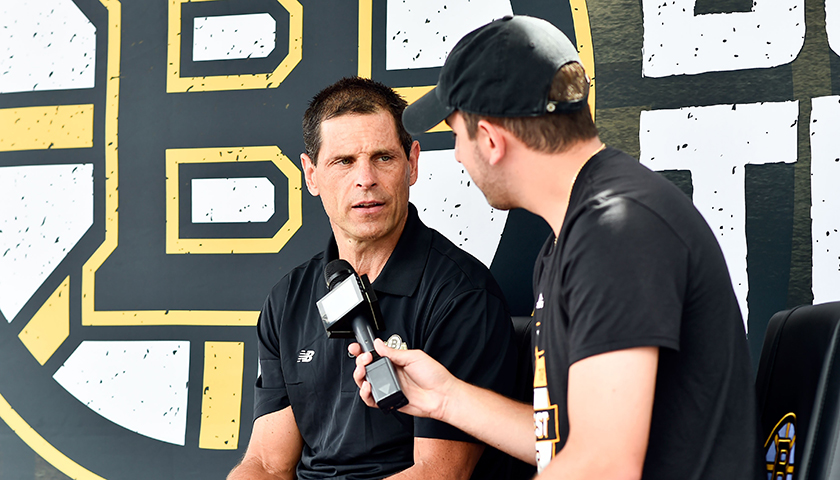 Don Sweeney and Eric Russo, who holds microphone, with large Bruins logo as backdrop