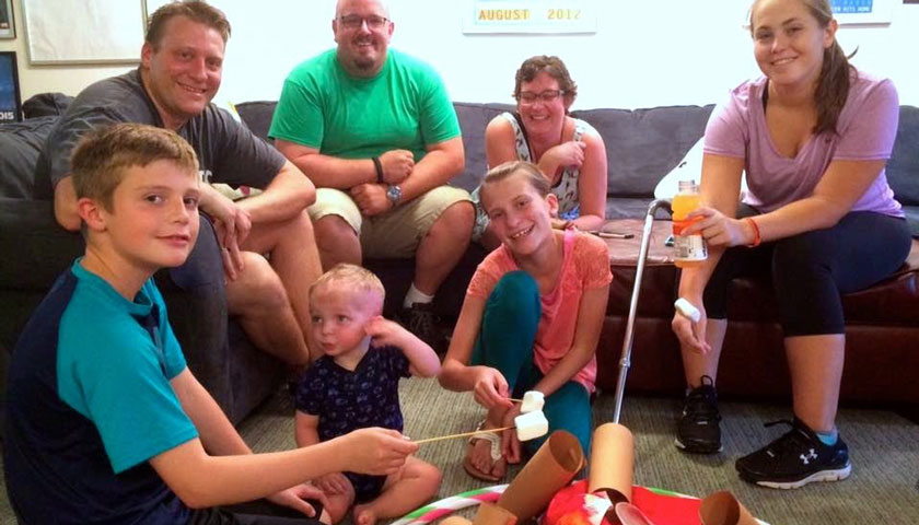 Children and parents gather and smile to roast marshmallows around a pretend campfire