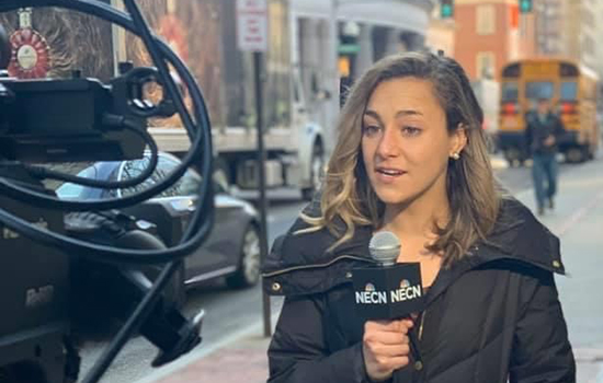 Amy Koczera in front of camera holding microphone 