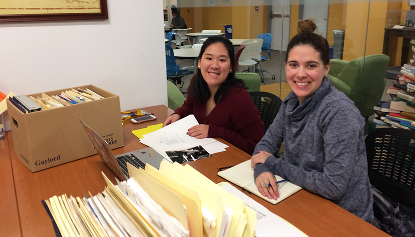 Two women with boxes of files at table in university archive