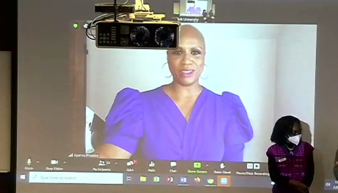 Ayanna Pressley appears on a Zoom screen behind student Ahria Ilyas in a Samia Academic Center classroom