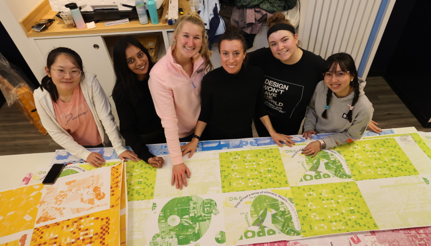 Master of Arts in Graphic Design students and professor Kristen Mallia pose with artwork in the Downtown Crossing space