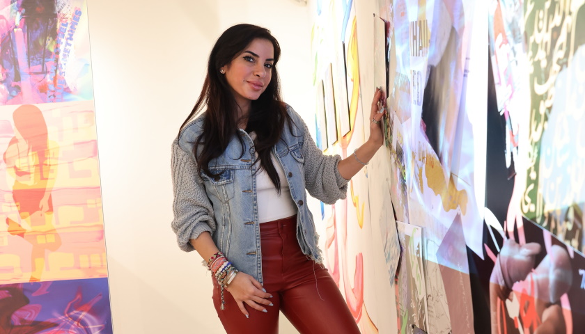 Ebby stands beside vibrant panels of her art
