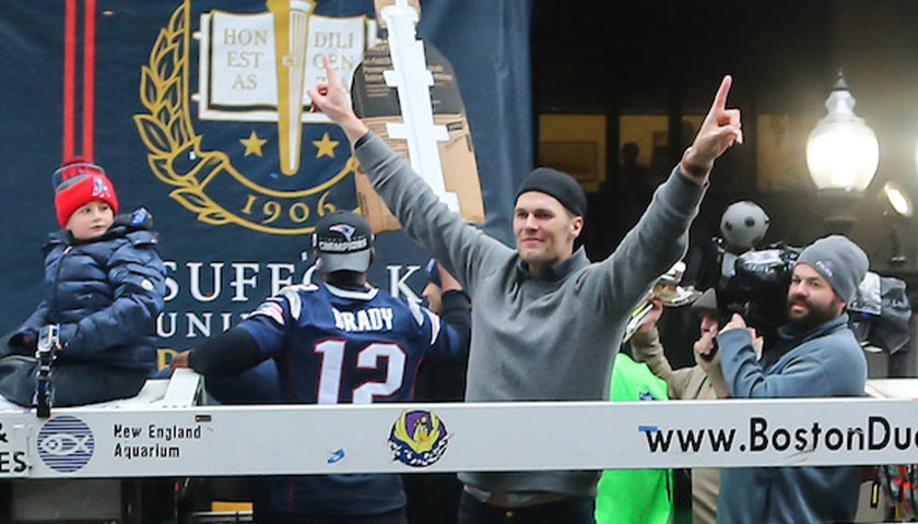 Tom Brady gives a "#1" sign from a duck boat at the Patriots Super Bowl parade in front of a crowd at Suffolk University
