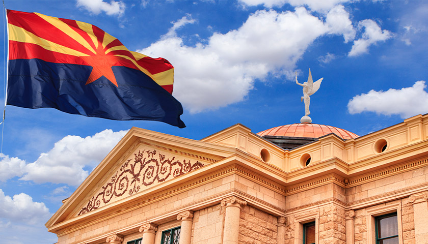 Arizona state flag flying in front the of the Arizona Statehouse