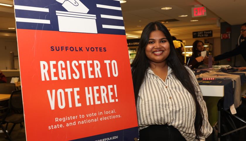 Syeeda Rahman smiles next to a Suffolk Votes voter registration sign