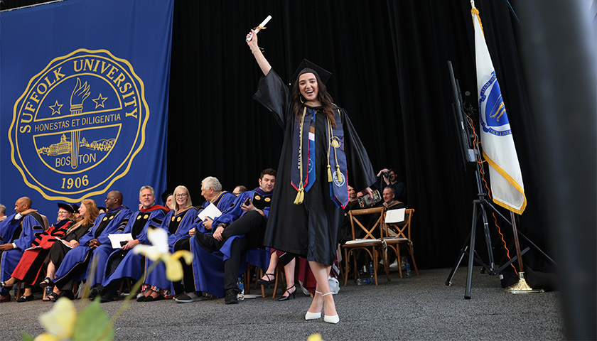 A new graduate of the Sawyer Business School waves her diploma at the audience at the 2023 Commencement